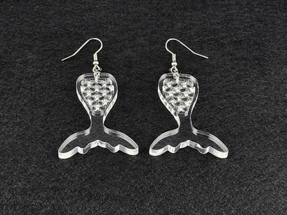 Pair of clear acrylic mermaid tail earrings photographed at an angle to show the laser-cut scale detail.