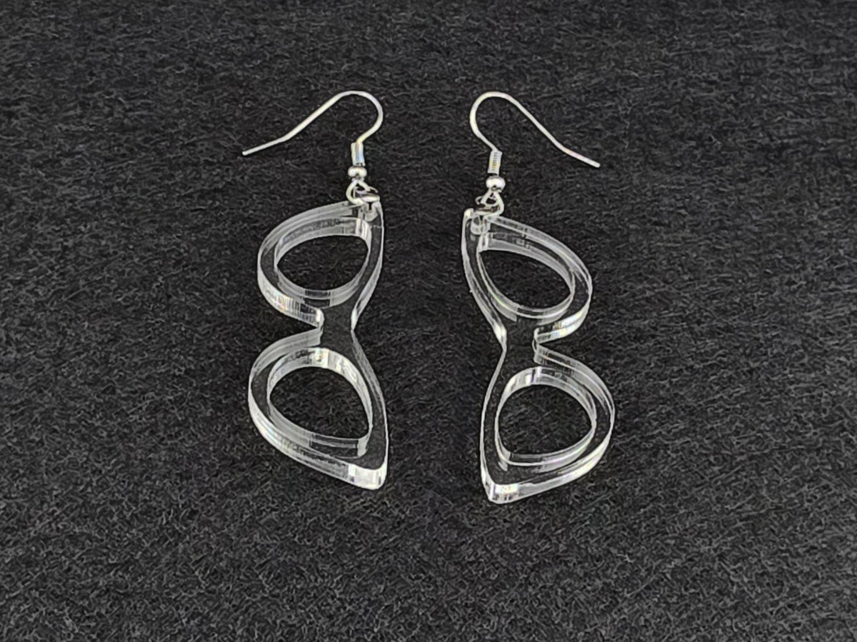 Clear acrylic cat-eye earrings shown at an angle on a charcoal background, highlighting the cut linework with no color tint.