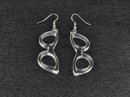 Clear acrylic cat-eye earrings shown at an angle on a charcoal background, highlighting the cut linework with no color tint.