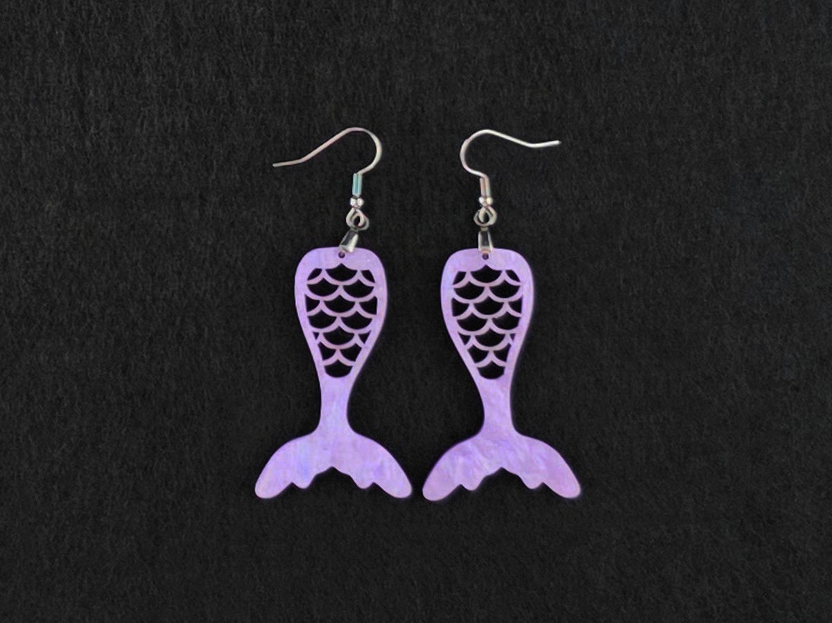Pair of lavender acrylic mermaid tail earrings with stainless steel French hook earwires, laid flat on a charcoal background.